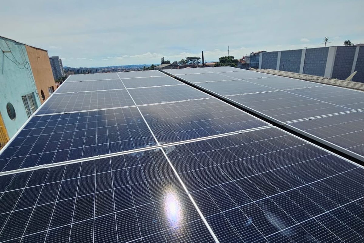 Telhado comercial coberto de módulos solares, com o horizonte da cidade ao
                  fundo