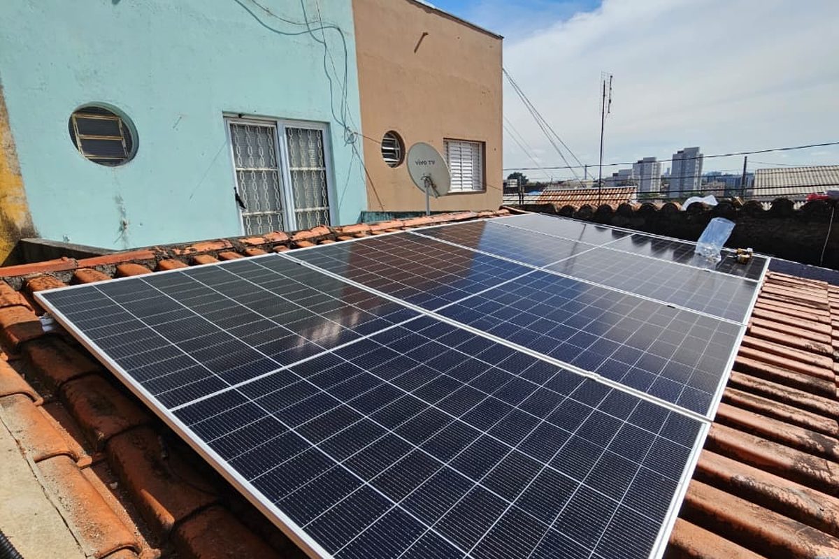 Módulos solares em telhado pequeno de casa urbana, entre paredes de vizinhos